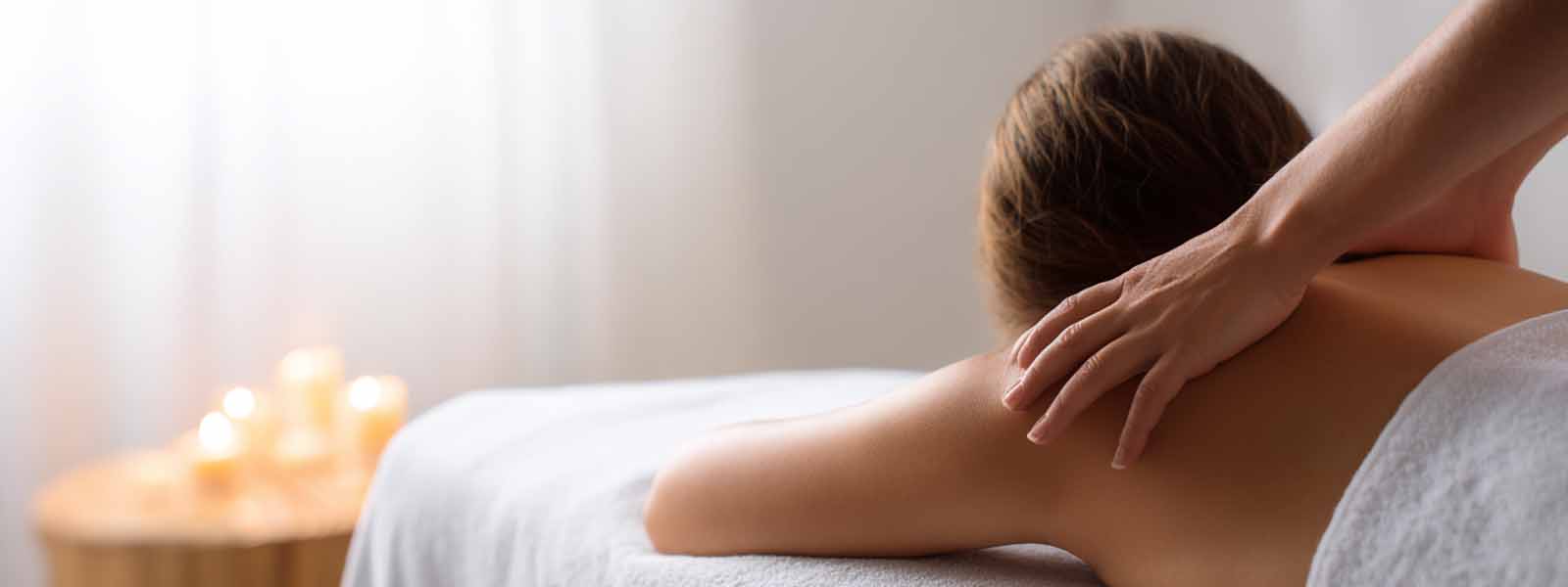 Therapist massaging a client’s back with candles glowing in the background during a stress relief massage in Reno