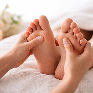 Close-up of a foot reflexology massage with therapist applying pressure to the soles of the feet on a soft white towel in a calm spa setting