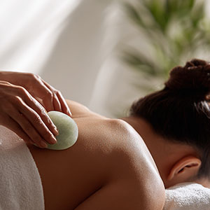 Gua sha tool applied to the upper back during a relaxing massage in a calm spa setting